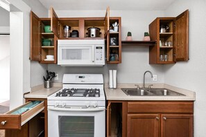 A compact kitchen with a gas stove, microwave, and wooden cabinets. - The Kangaroo - Bright Studio Apt, Walk to Mass Ave (Indianapolis)