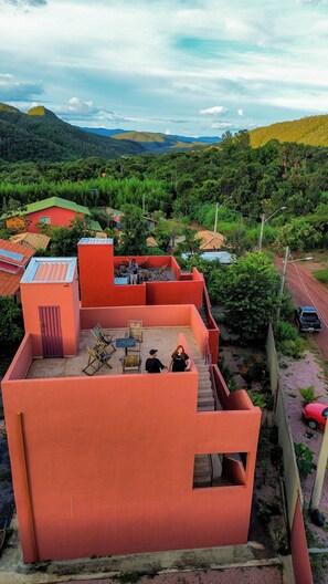 Edifici amb teulada vermella i zona de pati, envoltat de verdura exuberant i turons al fons.