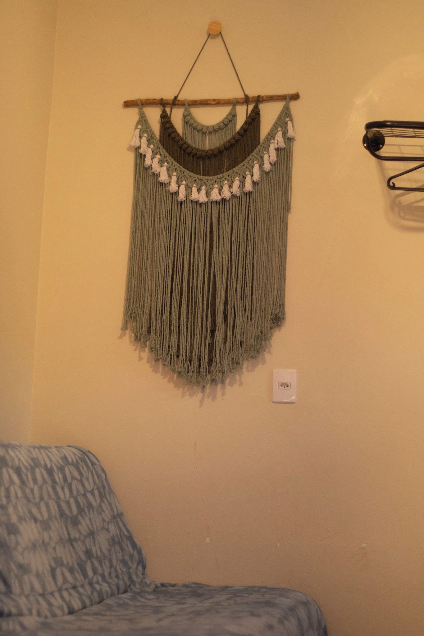 A wall with a macrame piece hanging on a wooden rod.