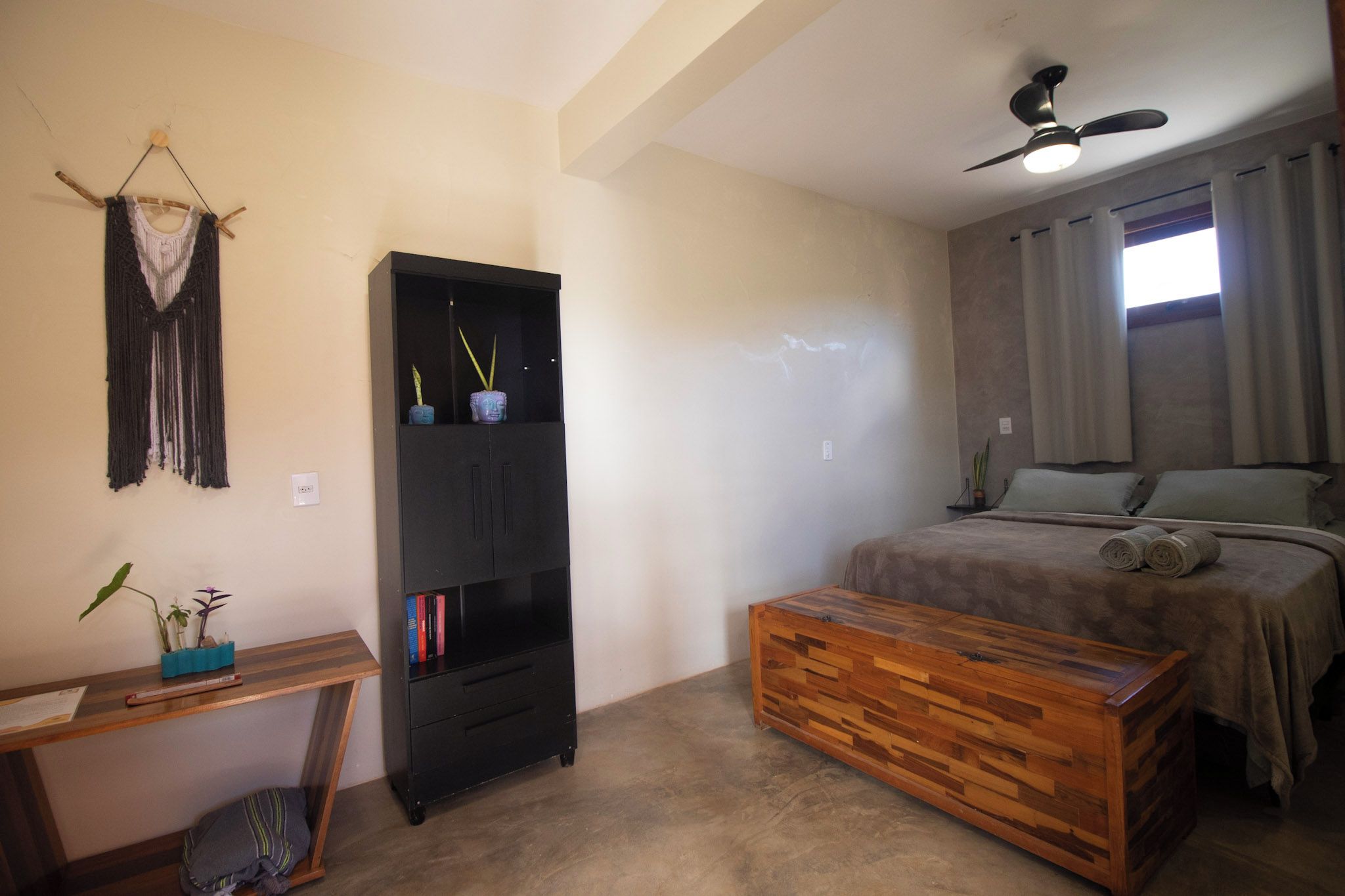 Een slaapkamer met een bed, een houten kist, een zwarte kast en een plafondventilator.