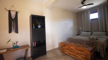 Een slaapkamer met een bed, een houten kist, een zwarte kast en een plafondventilator.