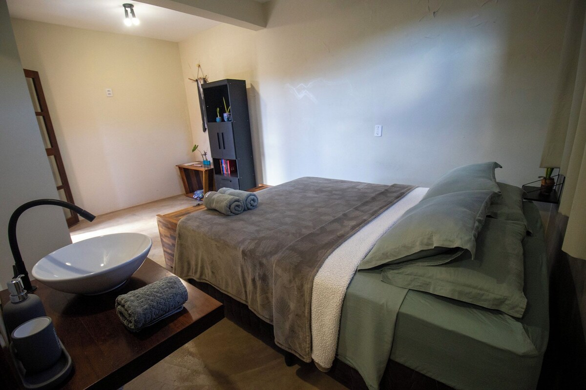 Un dormitorio con cama, mesita de noche, lavamanos amplio y armario.