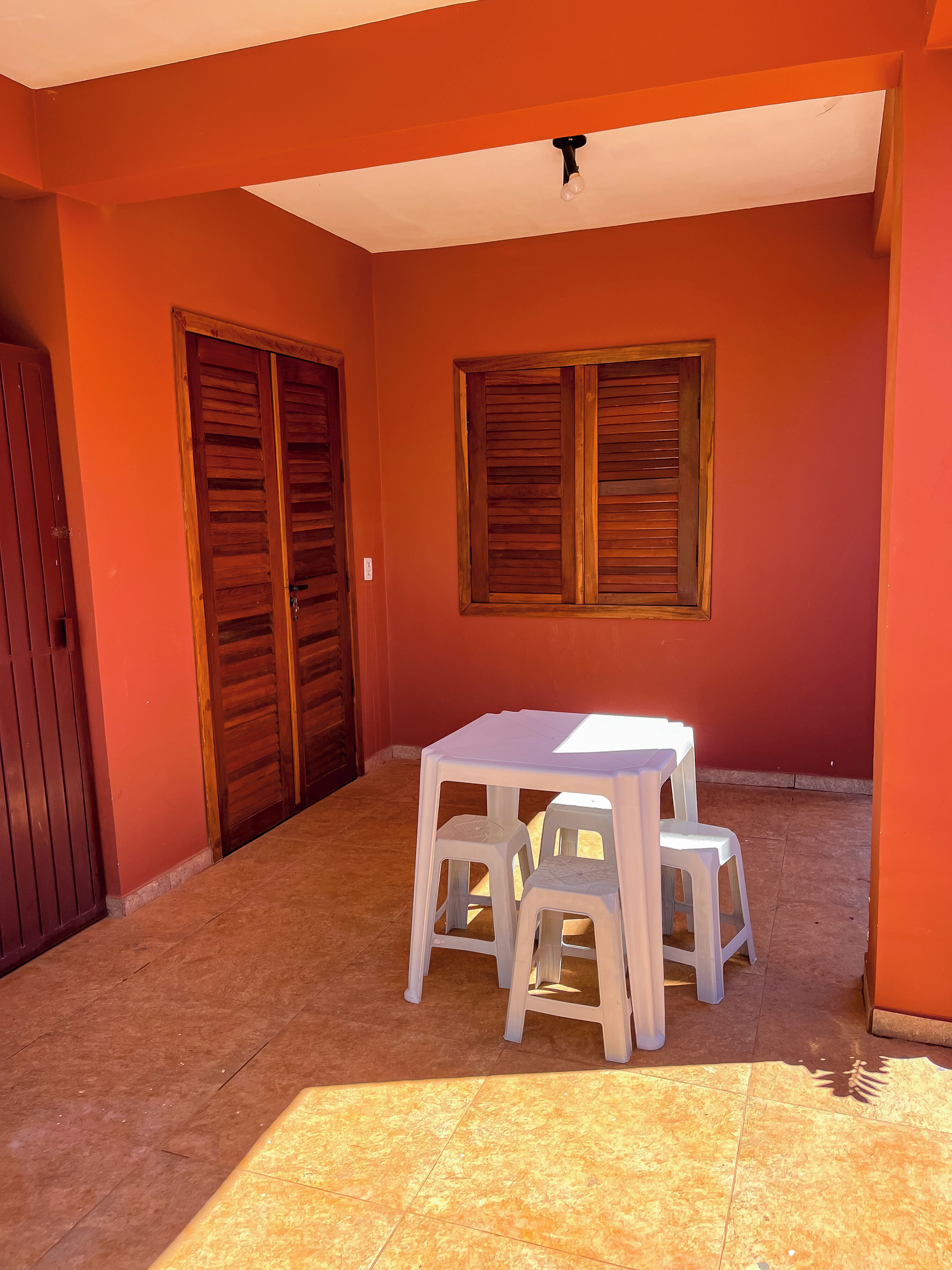 Una habitación con suelo de baldosas, una mesa con dos sillas y una ventana con contraventanas de madera.