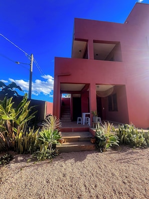 Un edifici modern de dos pisos amb façana vermella, una escala que condueix a l'entrada i un camí de grava.
