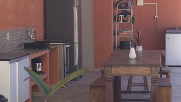 A compact kitchen with a refrigerator, stove, and sink. There is a dining table with benches and a potted plant.