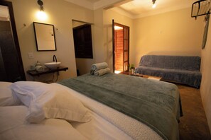 Habitación de hotel con dos camas, baño con lavamanos y zona de estar con sofá.