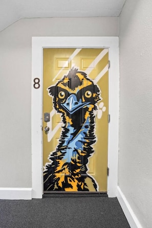 Una puerta con un mural vibrante de un pájaro, el número '8' en la pared y piso alfombrado.