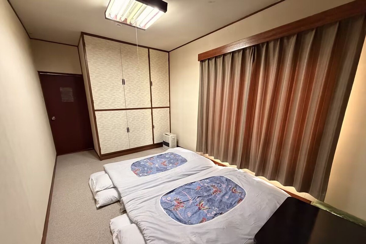 Una habitación de hotel con cama, armario, calefacción y ventana con cortinas.