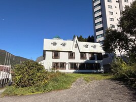 Un edificio de dos pisos con techo inclinado, varias ventanas y un balcón visible.