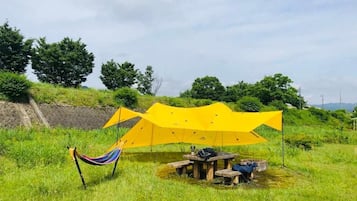 Una hamaca y una mesa montadas en un campo cubierto de hierba, con un toldo amarillo por encima.