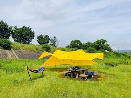 Una hamaca y una mesa montadas en un campo cubierto de hierba, con un toldo amarillo por encima.