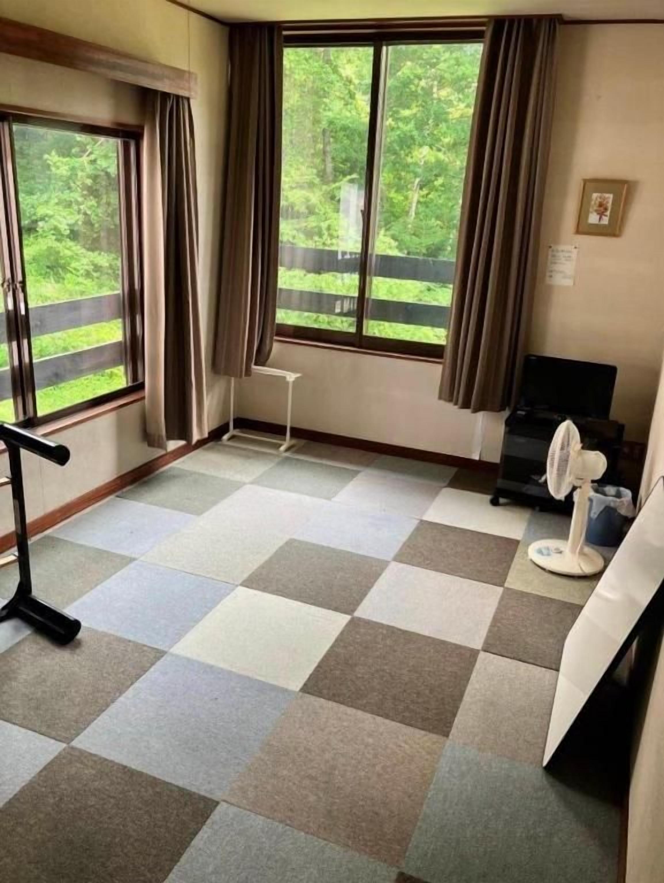 A room with a checkered floor, a desk, a chair, a fan, and a window with curtains.