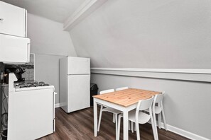 A compact kitchen with a gas stove, a white refrigerator, and a wooden table with white chairs. - The SugarGlider - King Bed Apt, Walk to Mass Ave (Indianapolis)