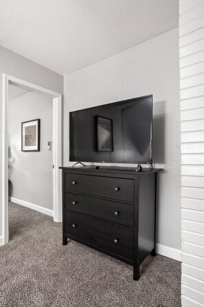 A room with a black dresser, a flat-screen TV mounted above it, and a framed picture on the wall. - The SugarGlider - King Bed Apt, Walk to Mass Ave (Indianapolis)