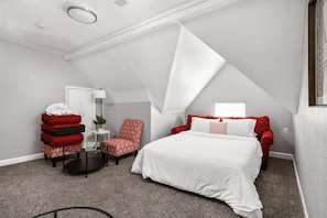 A compact room with a bed, a red armchair, a small table with a lamp, and a plant. - The SugarGlider - King Bed Apt, Walk to Mass Ave (Indianapolis)