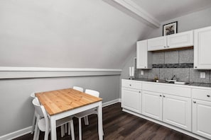 Uma cozinha compacta com armários brancos, uma mesa de madeira e um revestimento de azulejos.