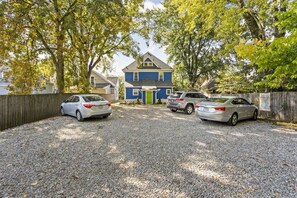 A gravel driveway with three cars parked, a blue house with a green door, and a wooden fence. - The SugarGlider - King Bed Apt, Walk to Mass Ave (Indianapolis)