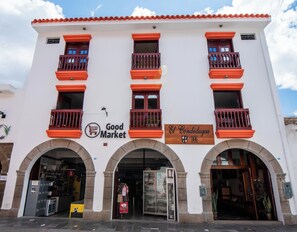 Un edificio con fachada blanca, balcones rojos y dos escaparates con los rótulos 'Good Market' y 'El Condegué'.