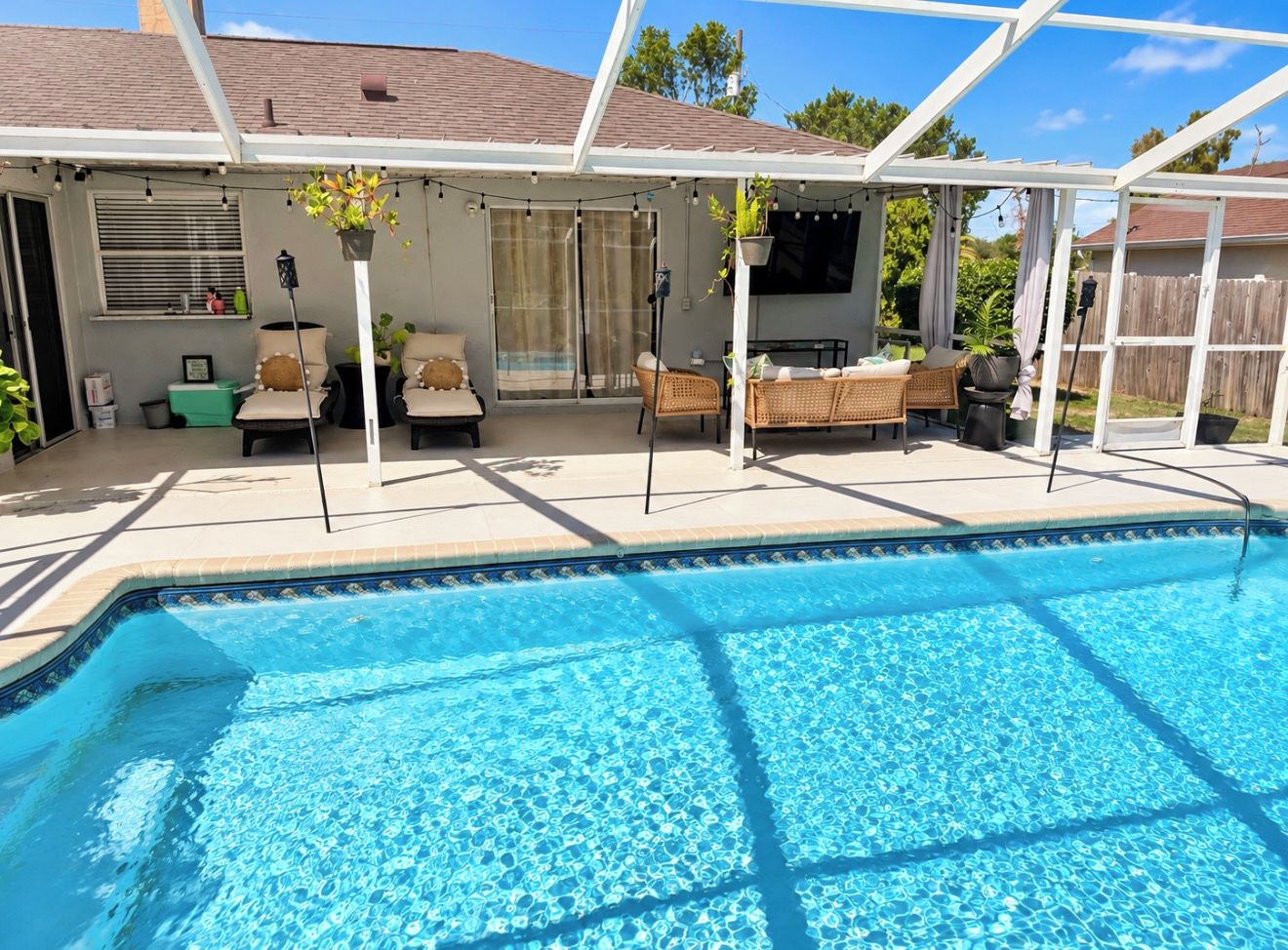 A swimming pool with a covered patio area, outdoor furniture, and potted plants.