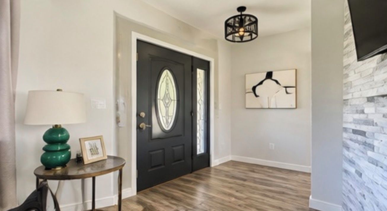 A hallway with a black door, a green lamp, a framed picture, and a wall-mounted artwork.