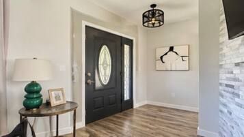A hallway with a black door, a green lamp, a framed picture, and a wall-mounted artwork.