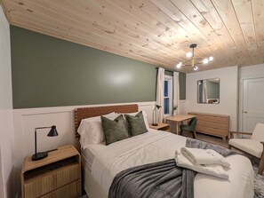 Ein Schlafzimmer mit Bett, Nachttischen, Schreibtisch, Stuhl, Spiegel und Deckenleuchte.