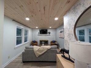 Ein gemütliches Wohnzimmer mit Kamin, einer Couch und einem an der Wand befestigten Fernseher.