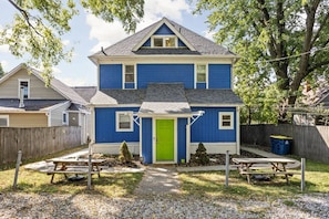 A two-story house with a green door, a fenced backyard, and picnic tables. - The Cockatoo - Two Queen Beds (Indianapolis)