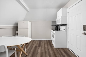 A compact kitchen with white appliances, a dining table, and a wooden floor. - The Cockatoo - Two Queen Beds (Indianapolis)