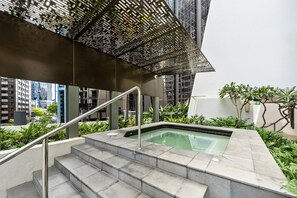 Ein moderner Poolbereich im Freien mit Stufen, die zu einem Pool führen, umgeben von Grünpflanzen und einer Metallkonstruktion darüber.