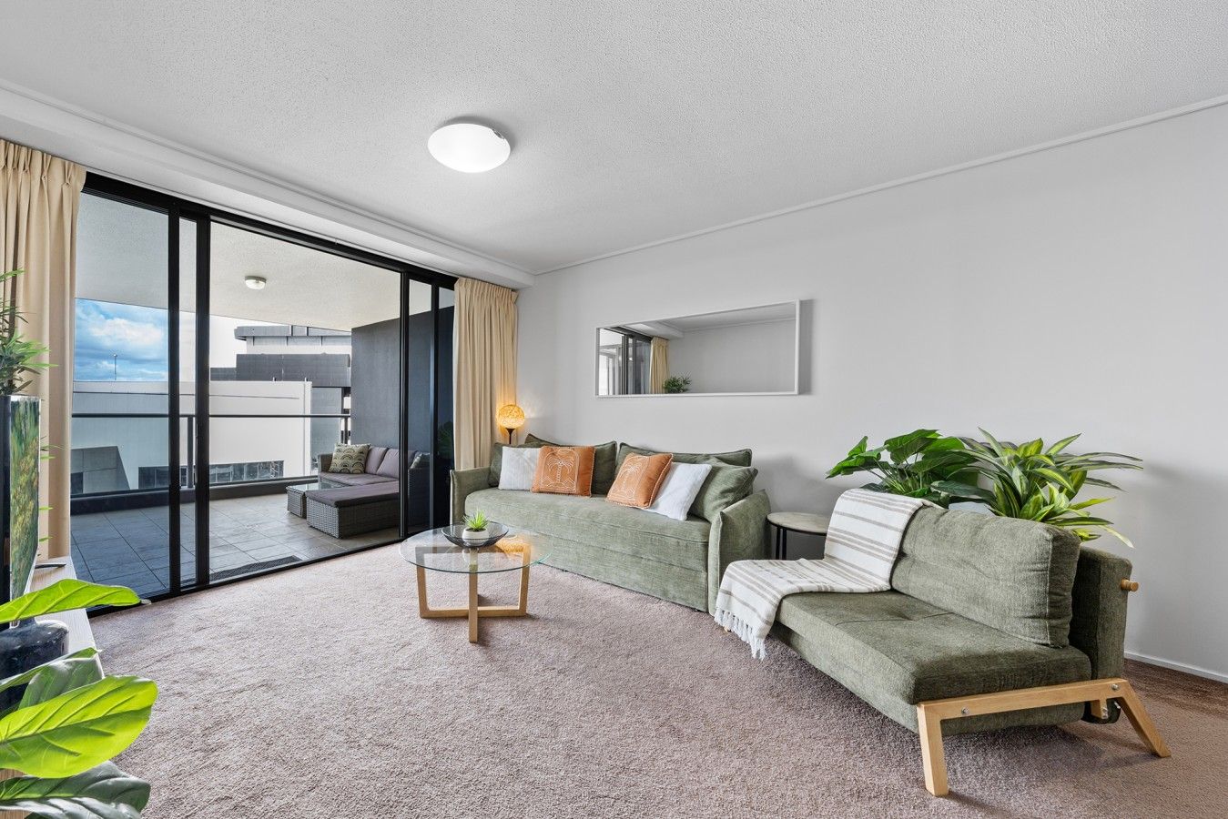 Ein modernes Wohnzimmer mit einem grünen Sofa, einem Glastisch und Blick auf einen Balkon.