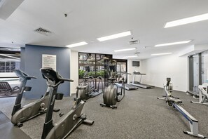 Ein Fitnessstudio mit verschiedenen Trainingsgeräten, darunter Laufbänder, Fahrräder und Crosstrainer.