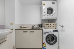 Une petite buanderie équipée d’un lave-linge, d’un évier et d’un meuble de rangement.