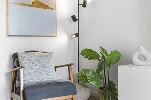 A modern room with a wooden chair, a floor lamp, a potted plant, and a piece of abstract art on the wall. - High-End 2BR Haven with Pool, Gym & Parking near South Bank & West End (South Brisbane)