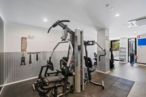 A gym with various exercise machines, a wall-mounted rack, and a patterned wall. - High-End 2BR Haven with Pool, Gym & Parking near South Bank & West End (South Brisbane)