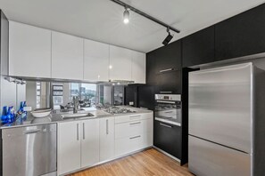 A modern kitchen with stainless steel appliances, a large refrigerator, and a view of the city. - High-End 2BR Haven with Pool, Gym & Parking near South Bank & West End (South Brisbane)