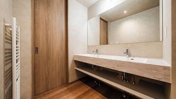 A modern bathroom with a wooden door, a white sink with a marble countertop, and a large mirror.