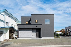 A modern two-story building with a garage, a flat roof, and a clear sky.