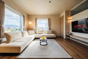 A modern living room with a sectional sofa, a coffee table, and a large TV screen displaying the Netflix logo.