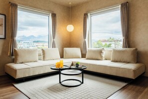 Una sala de estar moderna con un sofá color crema, dos mesitas auxiliares y vistas a montañas a través de amplios ventanales.