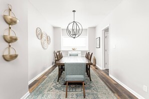 A dining area with a long table, chairs, a chandelier, and decorative wall art. - College Ave 6 Bedroom House Sleeps 14 (Indianapolis)