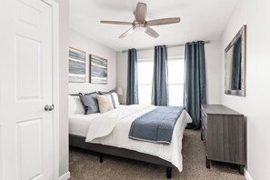 A bedroom with a bed, a ceiling fan, a dresser, and two windows with curtains. - College Ave 6 Bedroom House Sleeps 14 (Indianapolis)