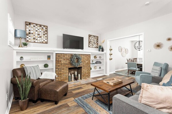 A modern living room with a fireplace, leather sofa, and a flat-screen TV on a white wall. - College Ave 6 Bedroom House Sleeps 14 (Indianapolis)