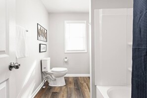 A bathroom with a toilet, a window, and a shower area. - College Ave 6 Bedroom House Sleeps 14 (Indianapolis)