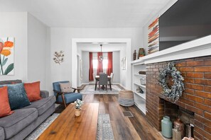 A living room with a fireplace, a dining area, and a hallway leading to another room. - College Ave 6 Bedroom House Sleeps 14 (Indianapolis)