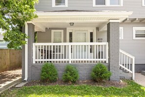 A residential house with a covered porch, a brick foundation, and a mailbox. - College Ave 6 Bedroom House Sleeps 14 (Indianapolis)