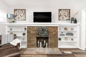 A living room with a brick fireplace, a flat-screen TV above it, and white shelving on either side. - College Ave 6 Bedroom House Sleeps 14 (Indianapolis)