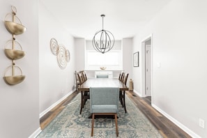 A dining area with a long table, chairs, a chandelier, and decorative wall art. - Cozy & Convenient, King Beds, Childrens Museum (Indianapolis)