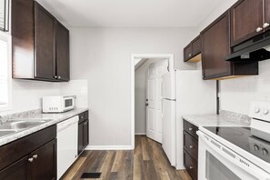 A kitchen with dark wooden cabinets, white appliances, and a wooden floor. - Cozy & Convenient, King Beds, Childrens Museum (Indianapolis)