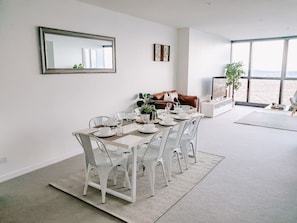 A dining area with a table set for four, white chairs, a large mirror, and a view through a large window. - Lavish Highend Skytower 2B/2B City Apt. Carpark (Brisbane City)